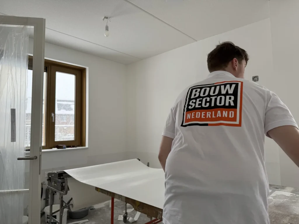 Behanger van Bouwsector Nederland trekt een baan vlies van de plaktafel in een kamer met witte wanden