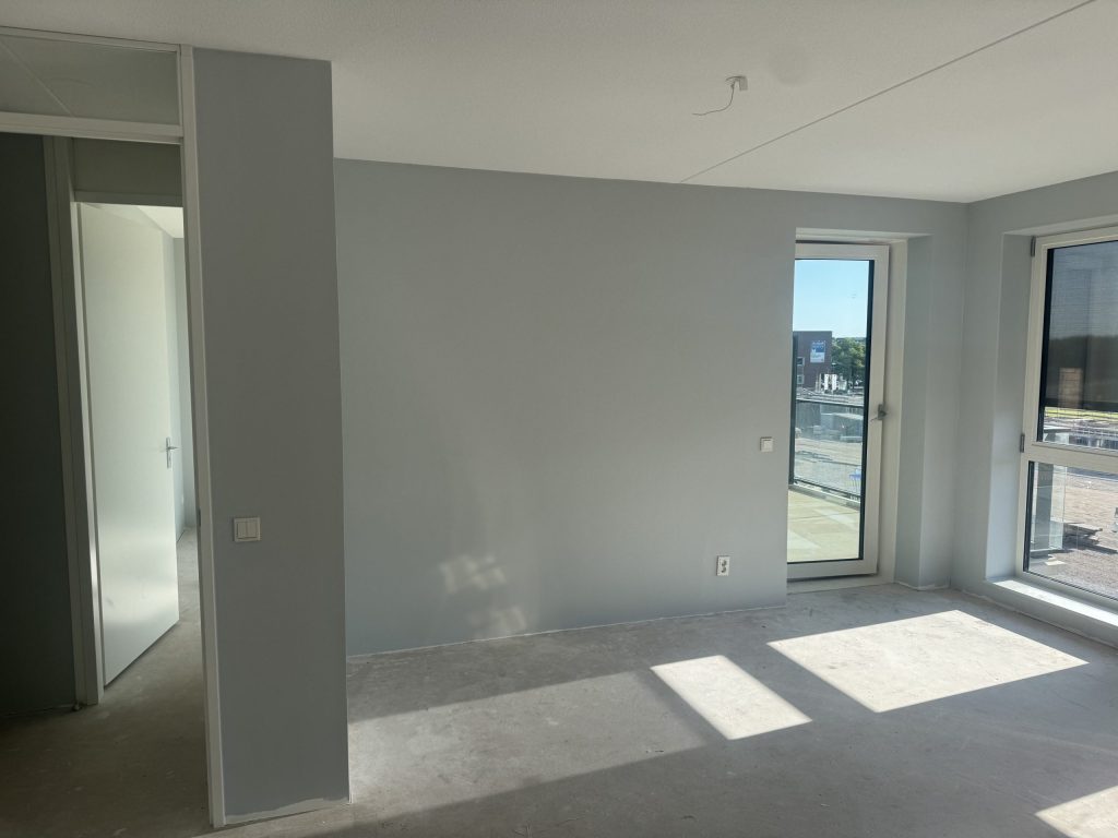 Lege kamer met strak afgewerkte lichtgrijze wanden en een balkondeur