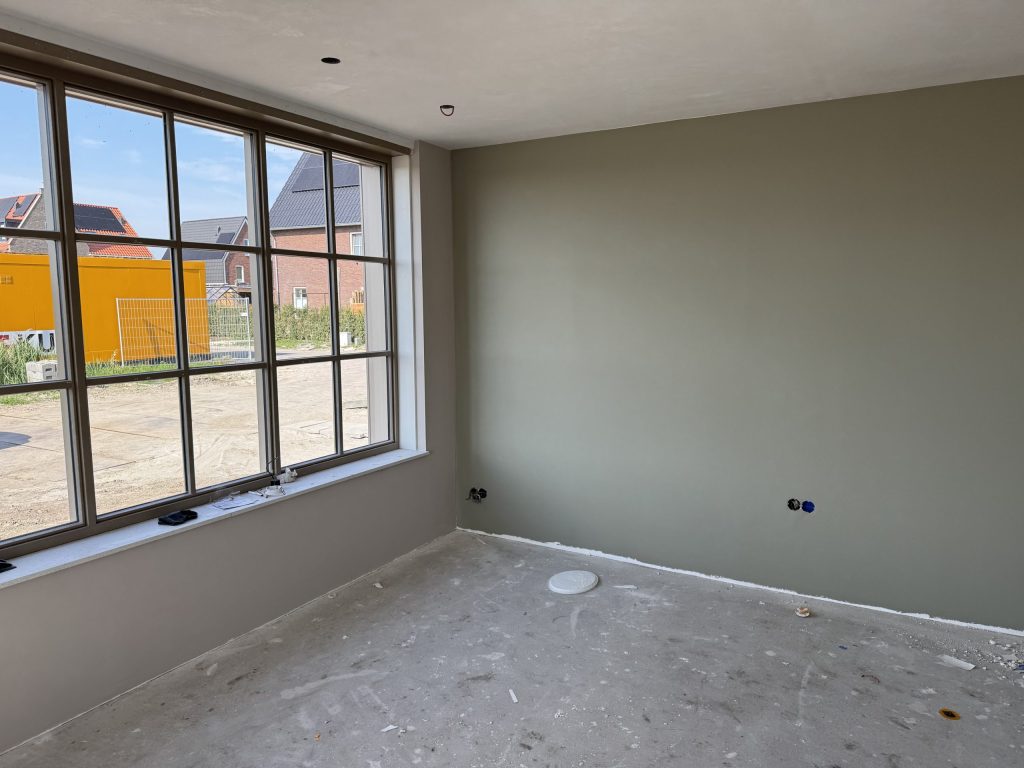 Kamer met een egaal afgewerkte grijsgroene wand en een groot raam met roedeverdeling