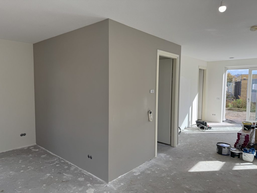 Pas afgewerkte grijze wand in een woonkamer, met verfemmers op de vloer